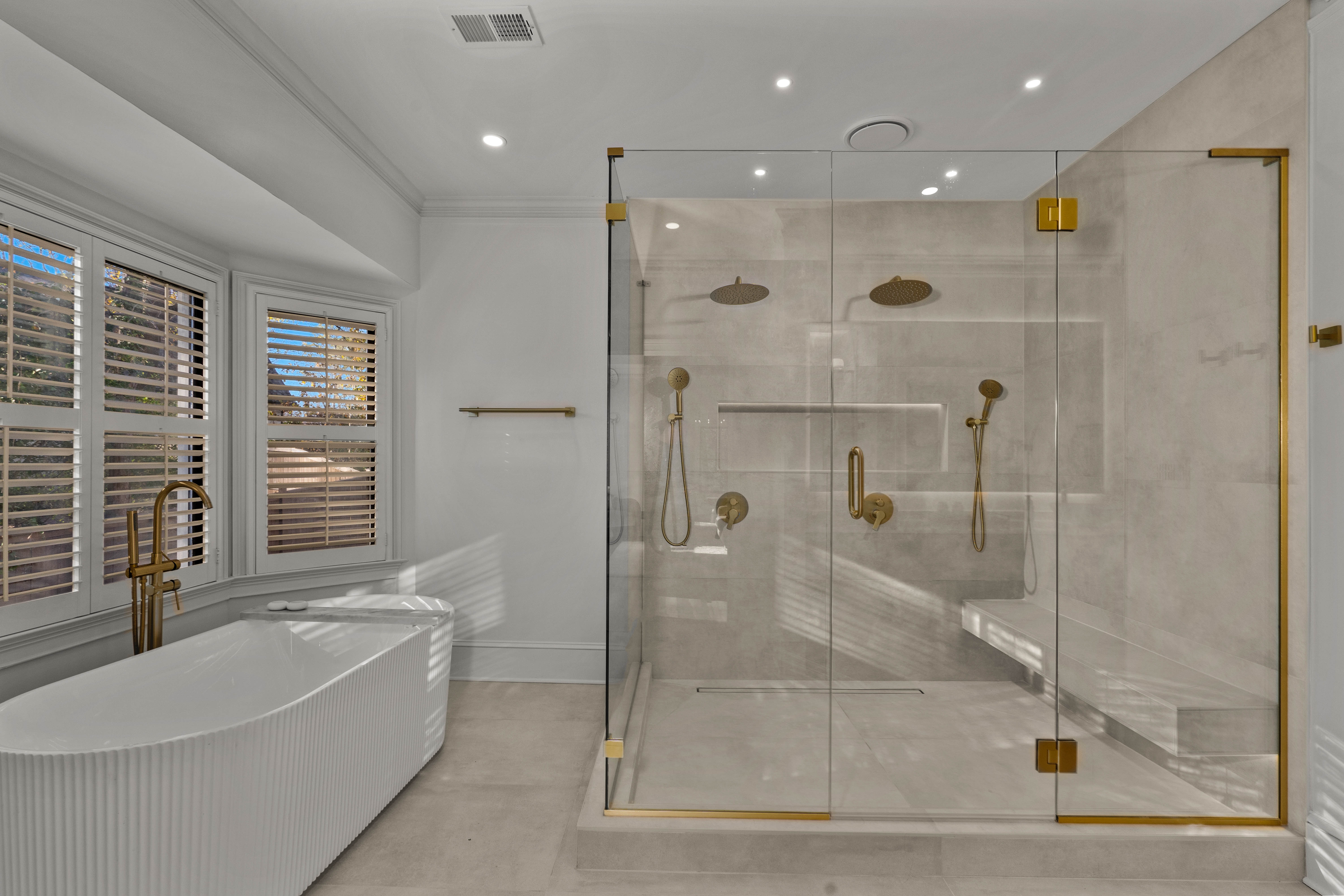 Primary bathroom after — freestanding tub, glass shower, brass fixtures