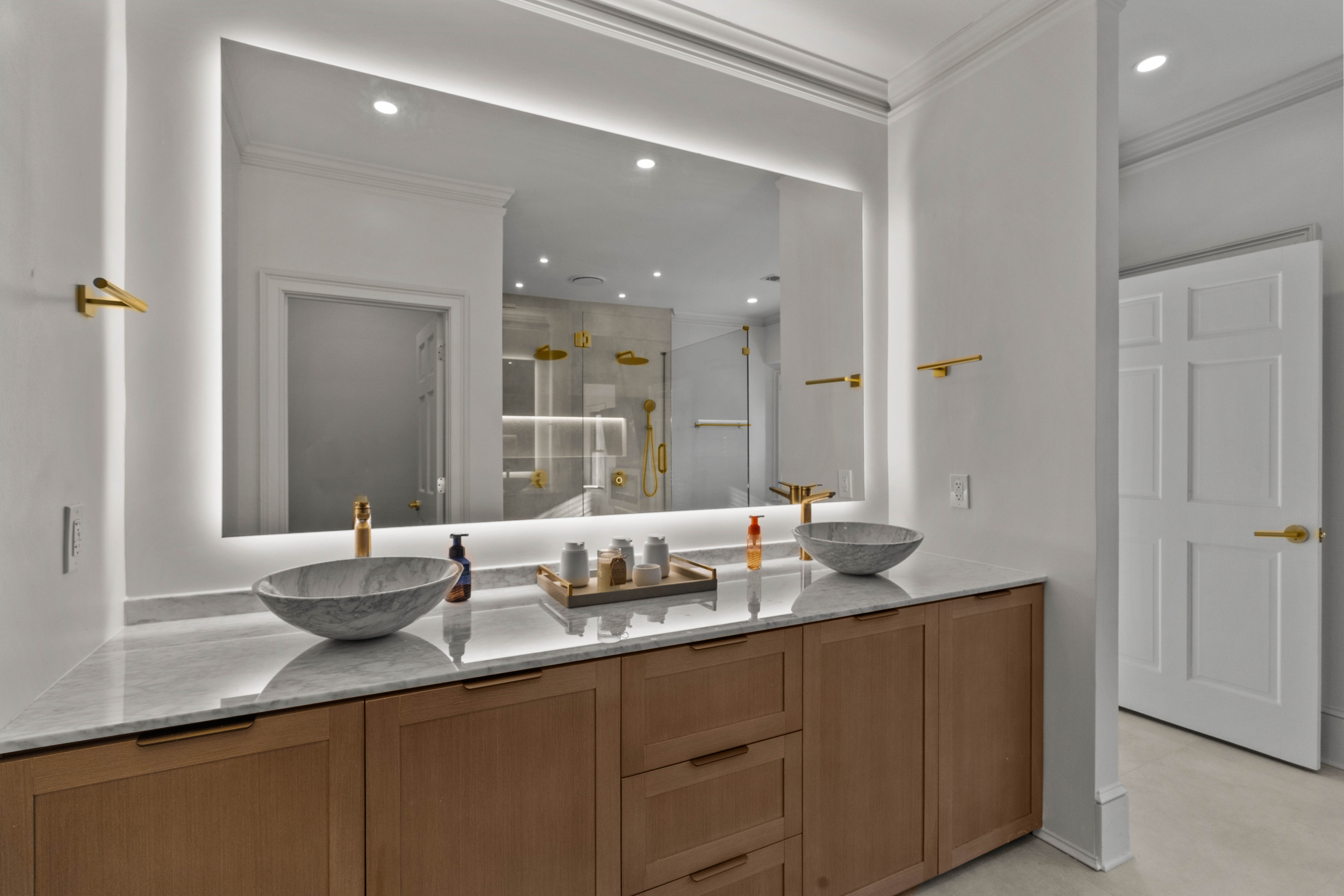 Primary vanity after — dual vessel sinks, backlit mirror, brass hardware