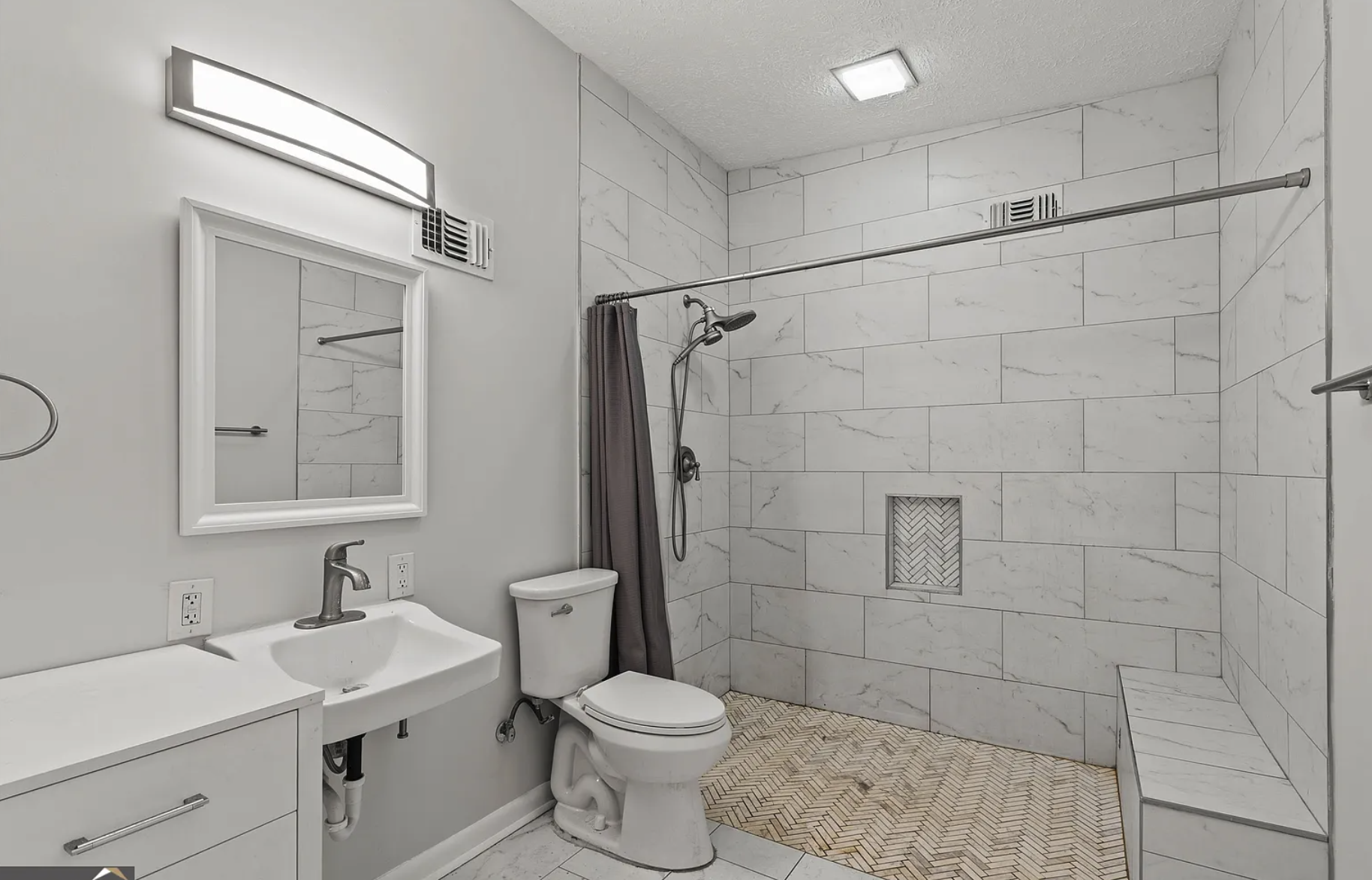 Bathroom after — marble tile shower, herringbone floor, white vanity