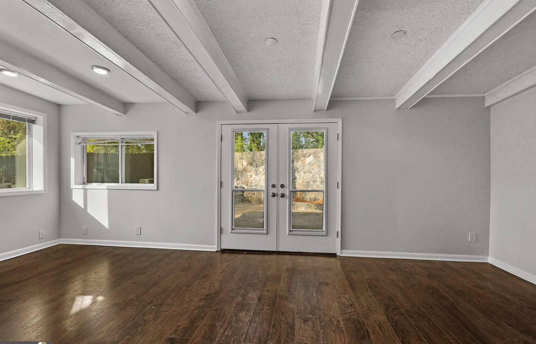 Room with french doors to backyard, painted beams, hardwood