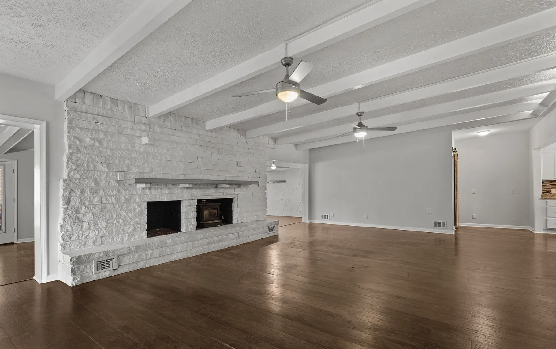 Great room after — painted white brick fireplace, exposed beams, hardwood