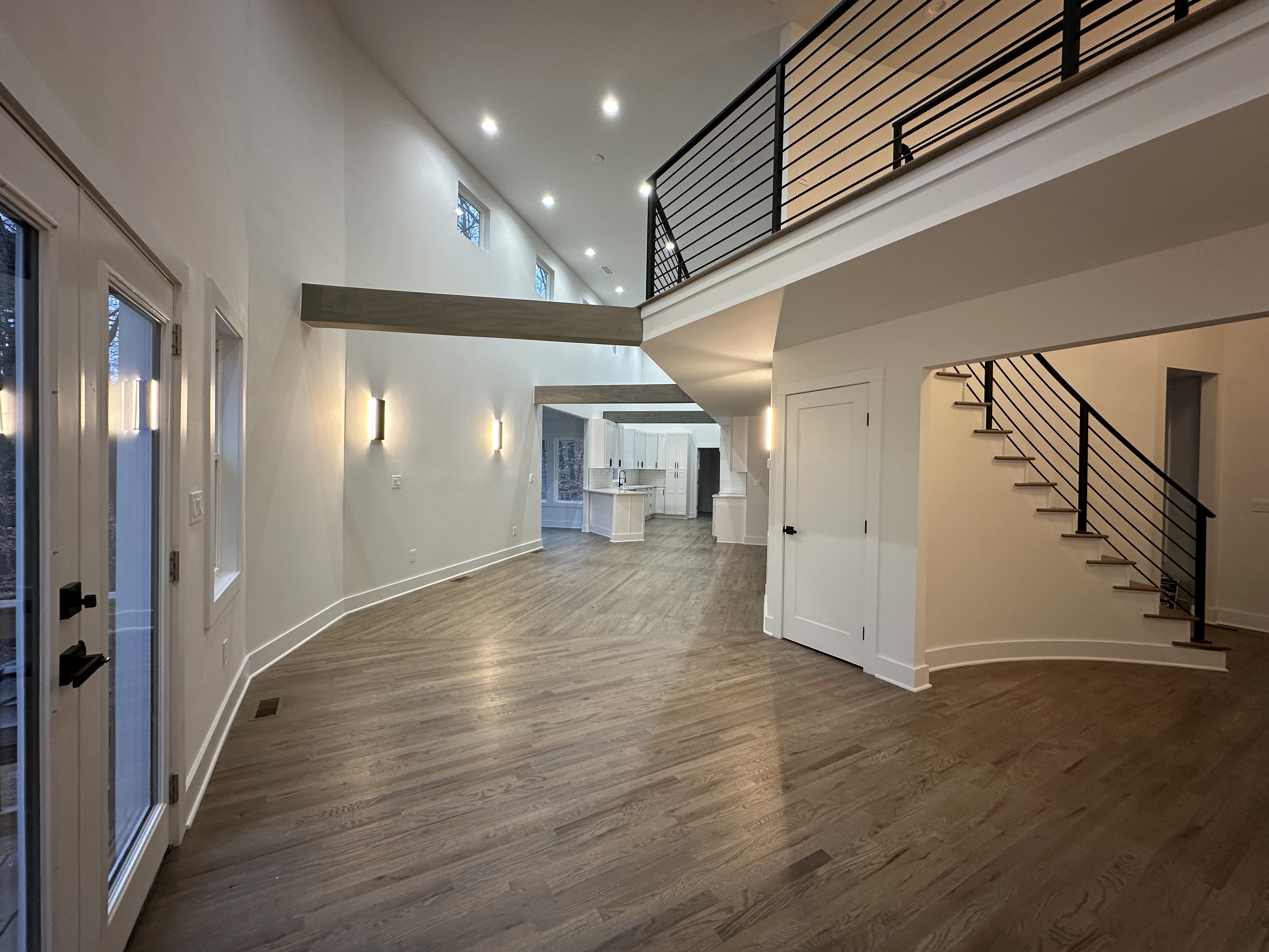 Open living with curved staircase, beam, sconces